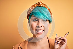 Young beautiful woman with blue fashion hair wearing casual diadem over yellow background very happy pointing with hand and finger
