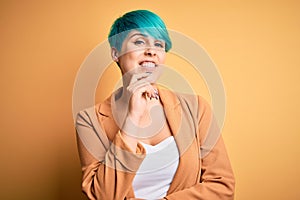 Young beautiful woman with blue fashion hair wearing casual jacket over yellow background looking confident at the camera with