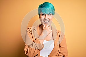 Young beautiful woman with blue fashion hair wearing casual jacket over yellow background looking confident at the camera smiling