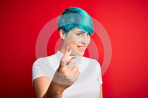 Young beautiful woman with blue fashion hair wearing casual t-shirt over red background Beckoning come here gesture with hand