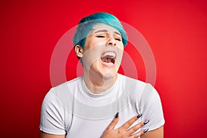 Young beautiful woman with blue fashion hair wearing casual t-shirt over red background smiling and laughing hard out loud because