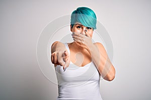 Young beautiful woman with blue fashion hair wearing casual t-shirt over white background laughing at you, pointing finger to the