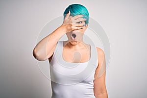 Young beautiful woman with blue fashion hair wearing casual t-shirt over white background peeking in shock covering face and eyes