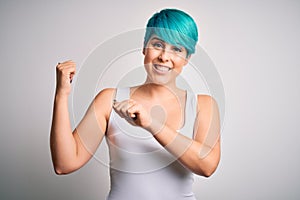 Young beautiful woman with blue fashion hair wearing casual t-shirt over white background Pointing to the back behind with hand