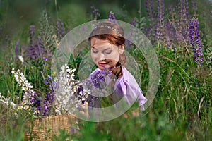 Young beautiful woman with bouquet of flowers in basket at summer nature sitting among grass. Pretty vintage girl in