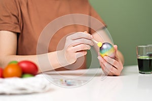 A young beautiful woman in a brown t-shirt paints Easter eggs in different colors. Preparing Easter Eve at home. Green