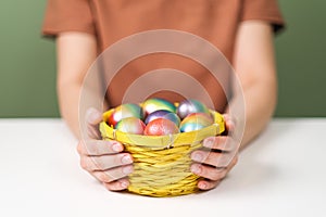 A young beautiful woman in a brown t-shirt paints Easter eggs in different colors. Preparing Easter Eve at home. Green