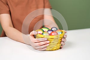 A young beautiful woman in a brown t-shirt paints Easter eggs in different colors. Preparing Easter Eve at home. Green