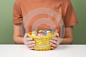 A young beautiful woman in a brown t-shirt paints Easter eggs in different colors. Preparing Easter Eve at home. Green