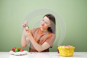 A young beautiful woman in a brown t-shirt paints Easter eggs in different colors. Preparing Easter Eve at home. Green