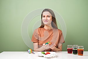 A young beautiful woman in a brown t-shirt paints Easter eggs in different colors. Preparing Easter Eve at home. Green