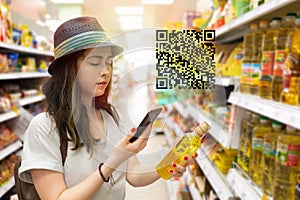 Young beautiful woman chooses a bottle of oil in the supermarket and checks the QR code on the label. The concept of modern