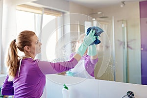 Young beautiful woman in cleaning mirror in bathroom