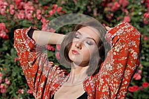 Young beautiful woman with closed eyes posing in the rose garden. Outdoor fashion portrait of a romantic girl with hard sunlight