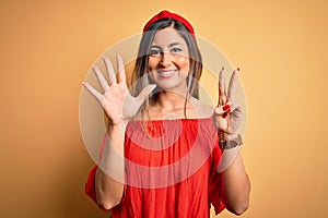 Young beautiful woman colorful summer style over yellow isolated background showing and pointing up with fingers number seven