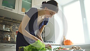 Young beautiful woman cook cutting the mushrooms on wooden board for pizza in the kitchen at home