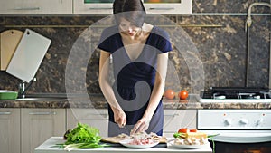 Young beautiful woman cook cutting the mushrooms on wooden board for pizza in the kitchen at home