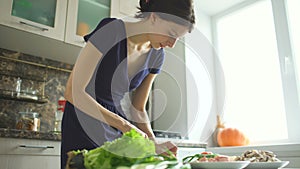 Young beautiful woman cook cutting the mushrooms on wooden board for pizza in the kitchen at home