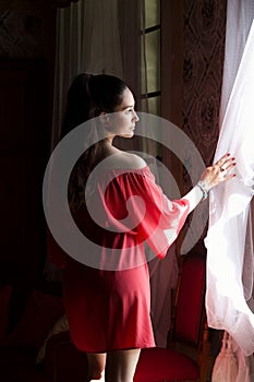Young beautiful woman in coral silk dress looking through a win photo