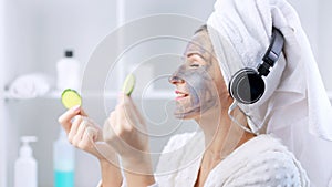 Young beautiful woman with cosmetic mask on her face and headphones relaxing in bathroom