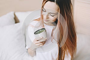 Young beautiful woman with cup of coffee or cacao in bed at home. Girl having breakfast in bed. Morning concept