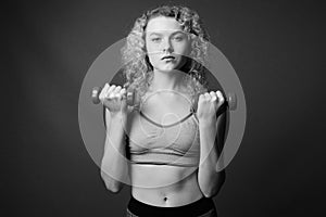 Young beautiful woman with curly blond hair ready for gym against gray background