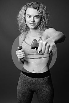 Young beautiful woman with curly blond hair ready for gym against gray background