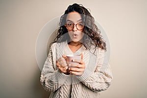 Young beautiful woman with curly hair drinking pink mug of coffee over white background scared in shock with a surprise face,