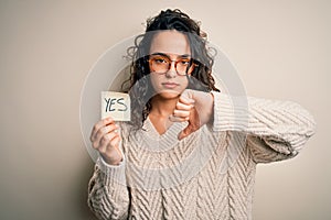 Young beautiful woman with curly hair holding reminder paper with yes word message with angry face, negative sign showing dislike