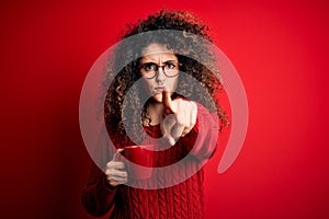 Young beautiful woman with curly hair and piercing drinking red cup of coffee pointing with finger to the camera and to you, hand