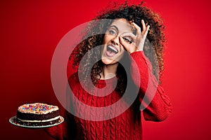 Young beautiful woman with curly hair and piercing holding plate with birthday cake with happy face smiling doing ok sign with