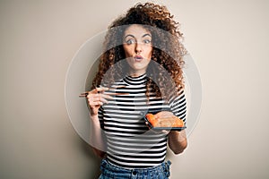 Young beautiful woman with curly hair and piercing holding tray with fresh sushi scared in shock with a surprise face, afraid and