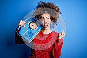 Young beautiful woman with curly hair and piercing listening to music using vintage radio screaming proud and celebrating victory