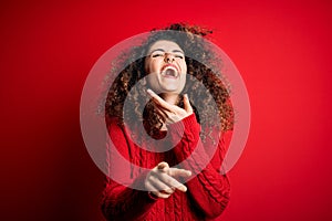 Young beautiful woman with curly hair and piercing wearing casual red sweater laughing at you, pointing finger to the camera with