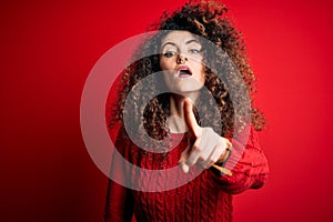 Young beautiful woman with curly hair and piercing wearing casual red sweater pointing displeased and frustrated to the camera,