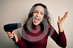 Young beautiful woman with curly hair using hair dryer over isolated white background very happy and excited, winner expression