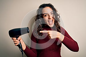 Young beautiful woman with curly hair using hair dryer over isolated white background very happy pointing with hand and finger