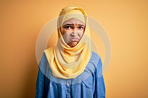 Young beautiful woman with curly hair wearing arab traditional hijab over yellow background depressed and worry for distress,