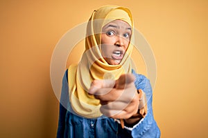 Young beautiful woman with curly hair wearing arab traditional hijab over yellow background pointing displeased and frustrated to