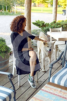 Young beautiful woman with curly hair, wearing in black dress, sead at terrace playing with her dog