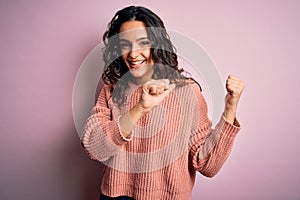 Young beautiful woman with curly hair wearing casual sweater over isolated pink background Pointing to the back behind with hand