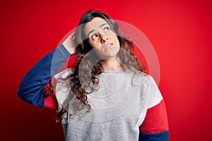 Young beautiful woman with curly hair wearing casual sweatshirt over isolated red background confuse and wondering about question