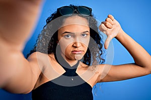 Young beautiful woman with curly hair wearing casual t-shirt making selfie by camera with angry face, negative sign showing