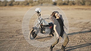 Young beautiful woman dances in the desert at sunset or sunrise. Motorcycle on background