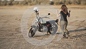 Young beautiful woman dances in the desert at sunset or sunrise and then sits on a motorcycle and ride away. Slow motion