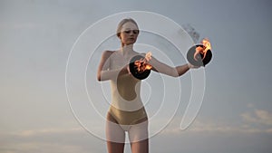 Young beautiful woman is dancing with fire wearing body suit on sunrise in the desert