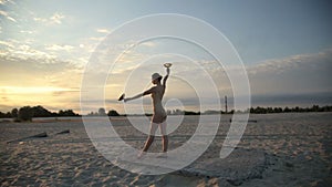 Young beautiful woman is dancing with fire wearing body suit on sunrise in the desert