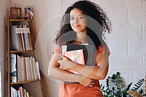 Young beautiful woman with dark curly hair in T-shirt holding books in hands dreamily looking in camera with bookshelf