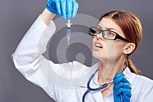 Young beautiful woman on a dark gray background holds a syringe with glasses, doctor, medicine, medical gown