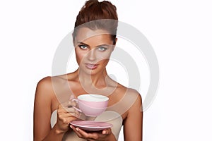 Young beautiful woman with dark hair picked up holding a ceramic cup and saucer pale pink drink tea or coffee on a white back
